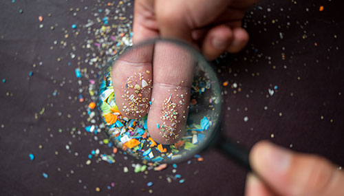 Close-up on micro plastic particles on the fingers under a magnifying glass